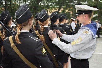 Ученица военного училища принимает помощь молодого моряка в корректировке своих погонов.