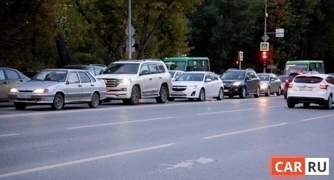 В городе, на дороге, происходит движение, где машины останавливаются, ожидая смены сигнала светофора на красный.